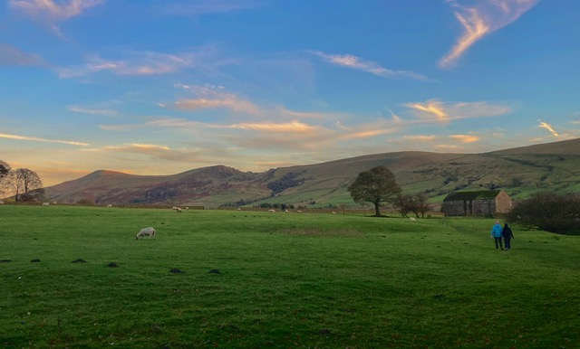 Scenic landscape with rolling hills, lush green fields, and two walkers enjoying the tranquil countryside at sunset