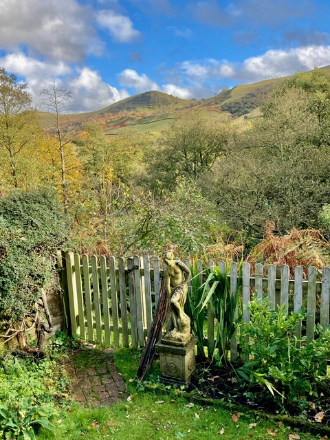 Scenic garden view with lush greenery, stone statue, and mountain backdrop in a luxury cottage setting