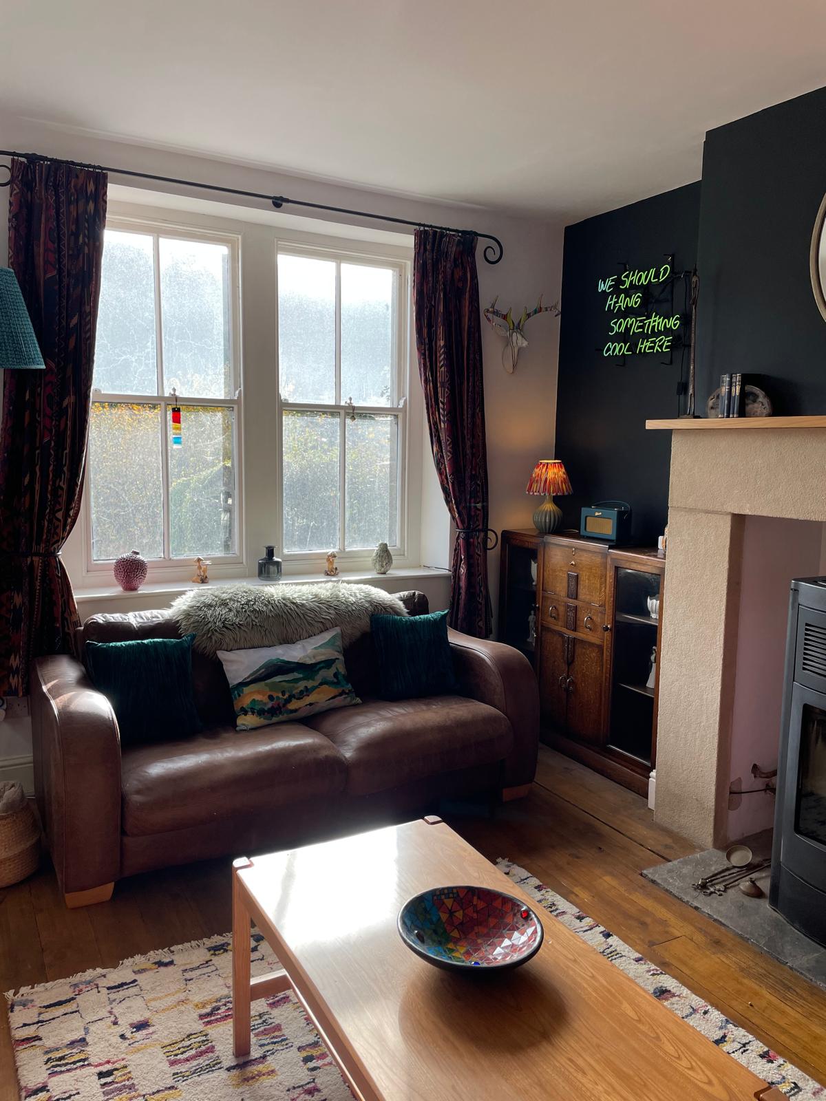 Cozy luxury cottage living room with a leather sofa, wooden furniture, and large windows overlooking a garden