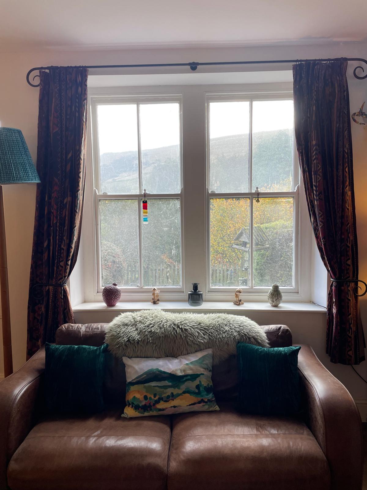 Cozy living room with a leather sofa, decorative cushions, and large windows showcasing stunning mountain views