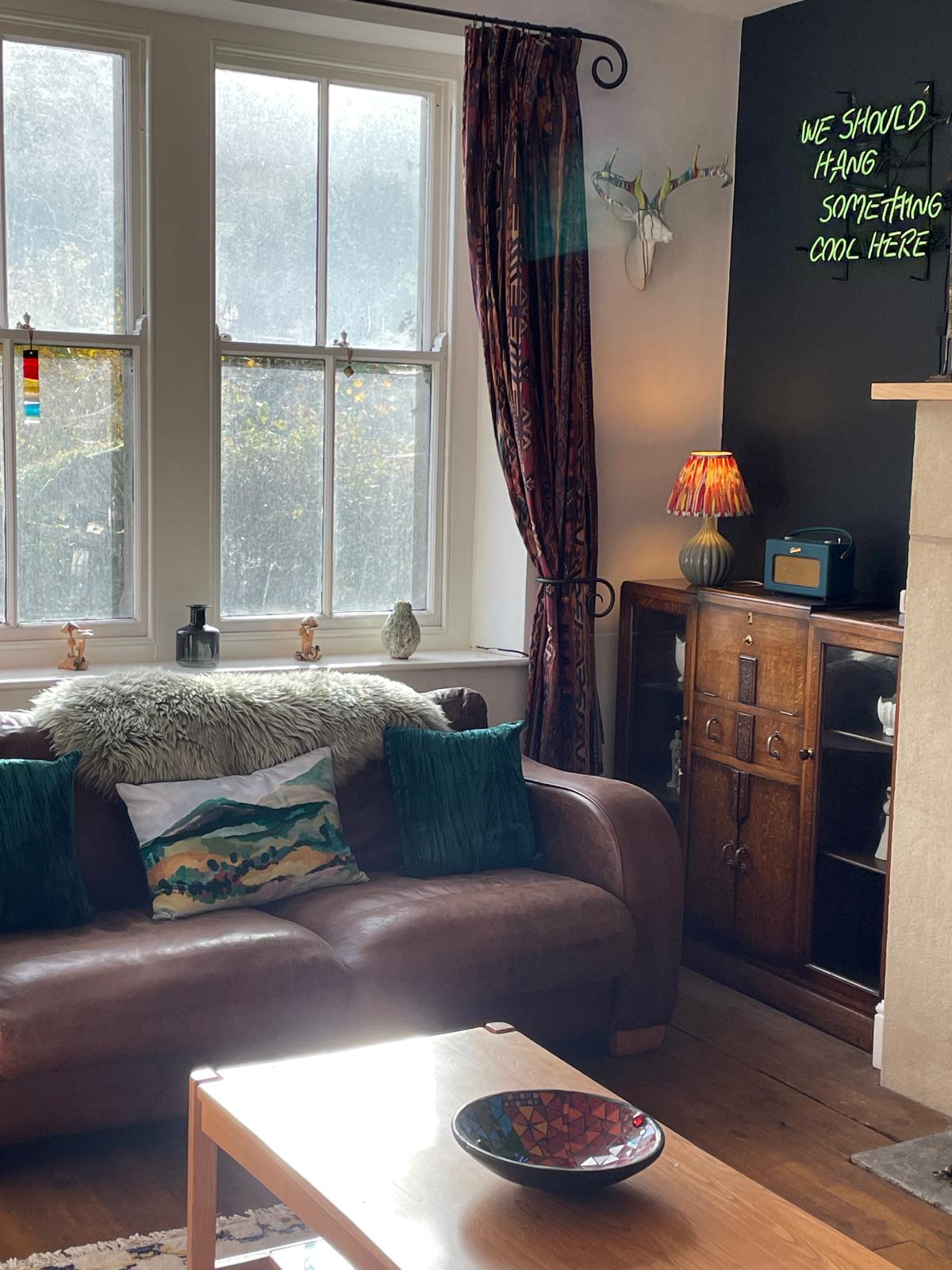Cozy luxury cottage living room with a brown leather sofa, decorative pillows, vintage cabinet, and stylish wall art