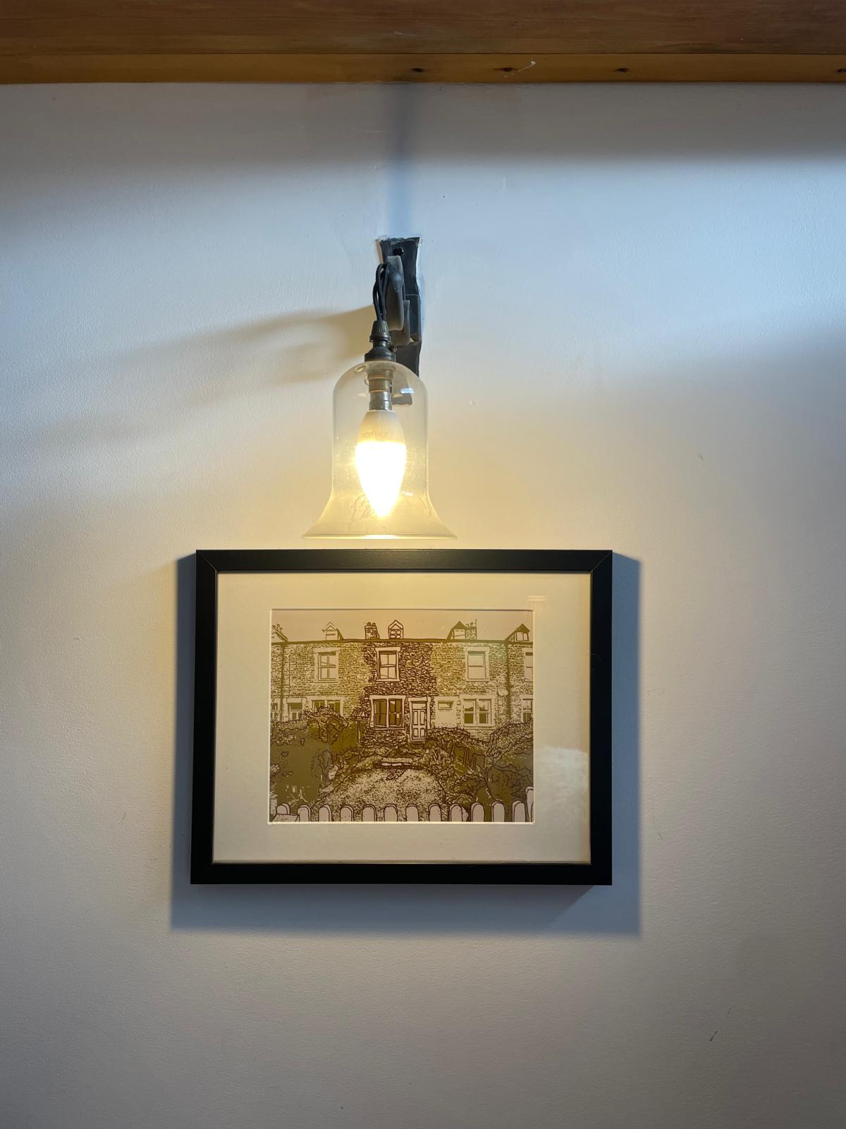 Framed artwork of a cottage with a stylish pendant light above, enhancing the cozy luxury atmosphere
