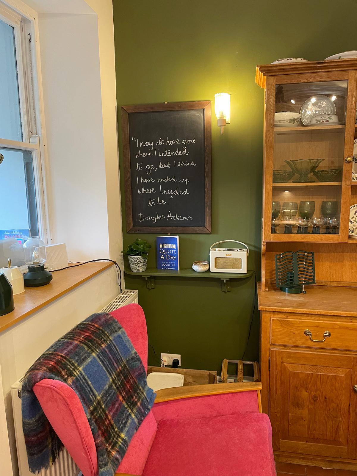 Cozy cottage corner with a pink chair, wooden cabinet, and decorative chalkboard, featuring stylish decor and warm ambiance