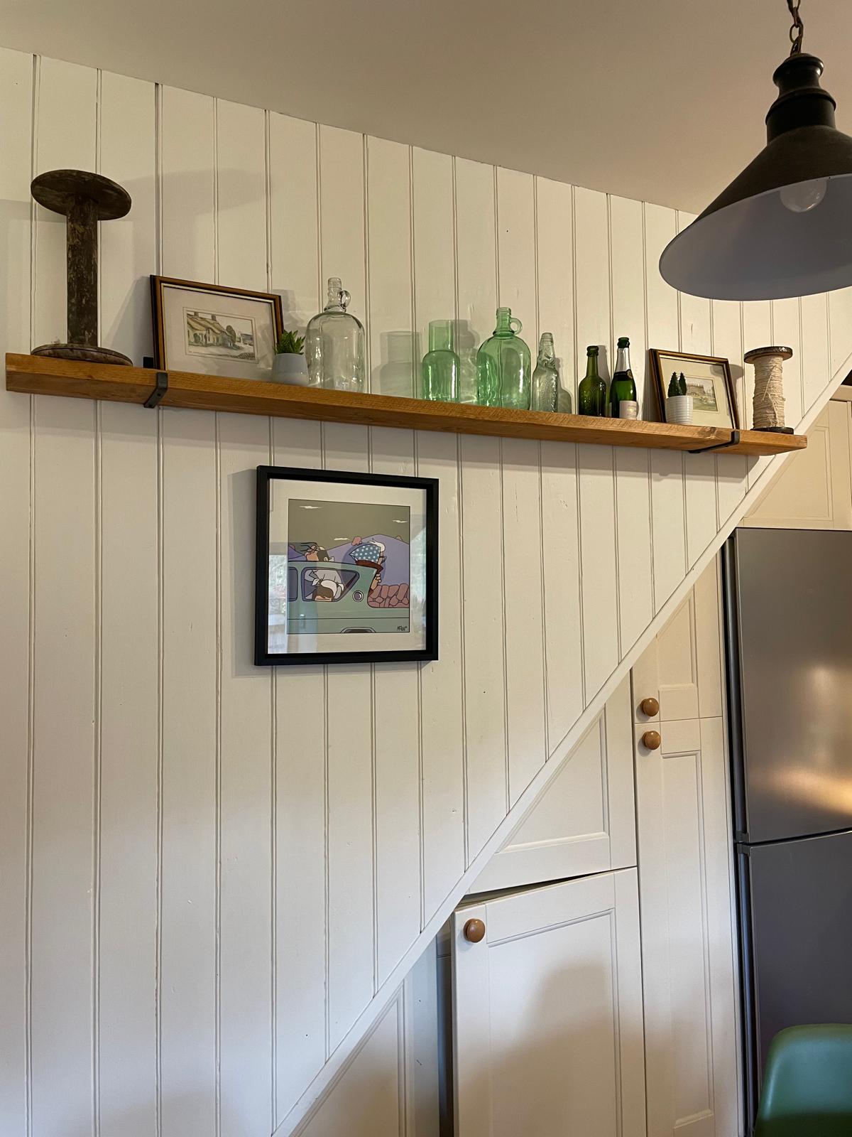 Charming cottage interior with wooden shelf, decorative glassware, artwork, and modern kitchen appliances