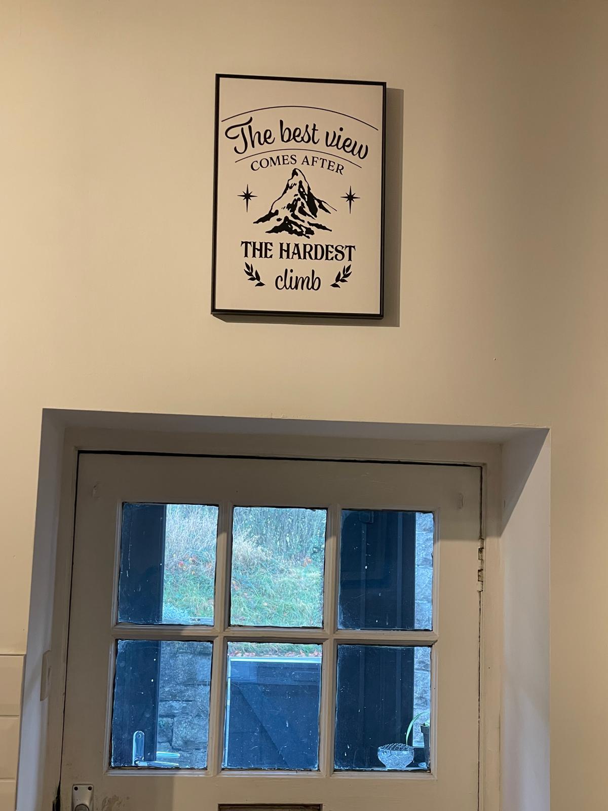 Framed motivational sign above a rustic door, with a view of natural light filtering into a cozy cottage interior