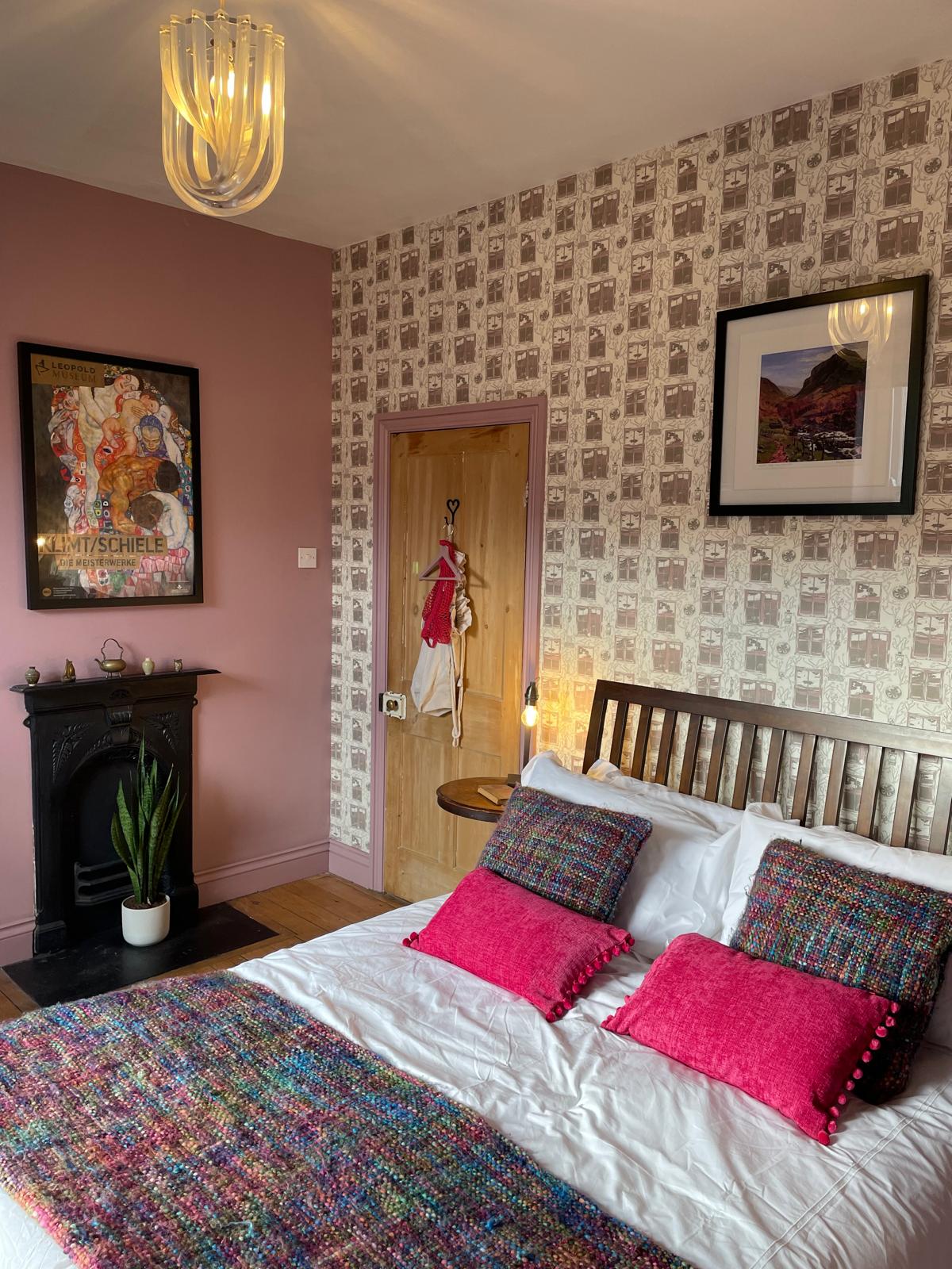 Luxury cottage bedroom featuring a cozy bed, vibrant decor, stylish wallpaper, and a decorative fireplace