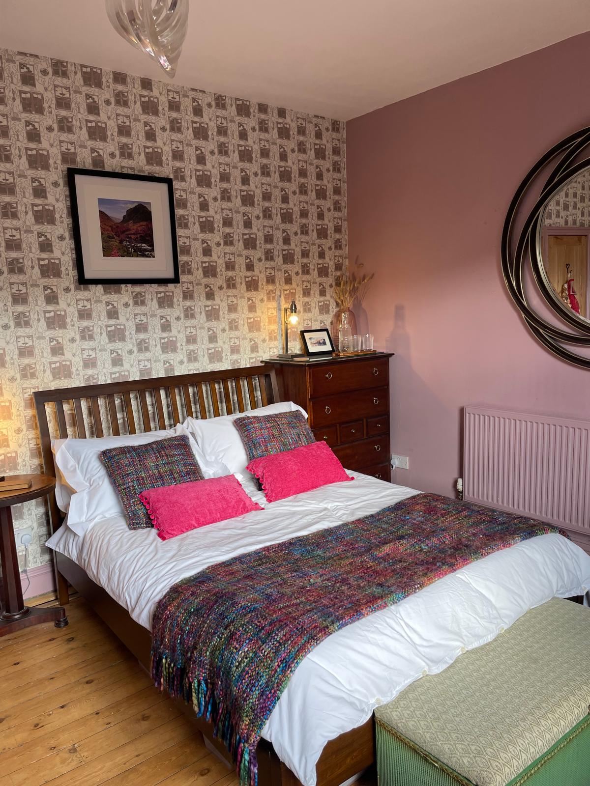 Cozy luxury bedroom with a wooden bed, colorful throw, stylish decor, and vintage wallpaper