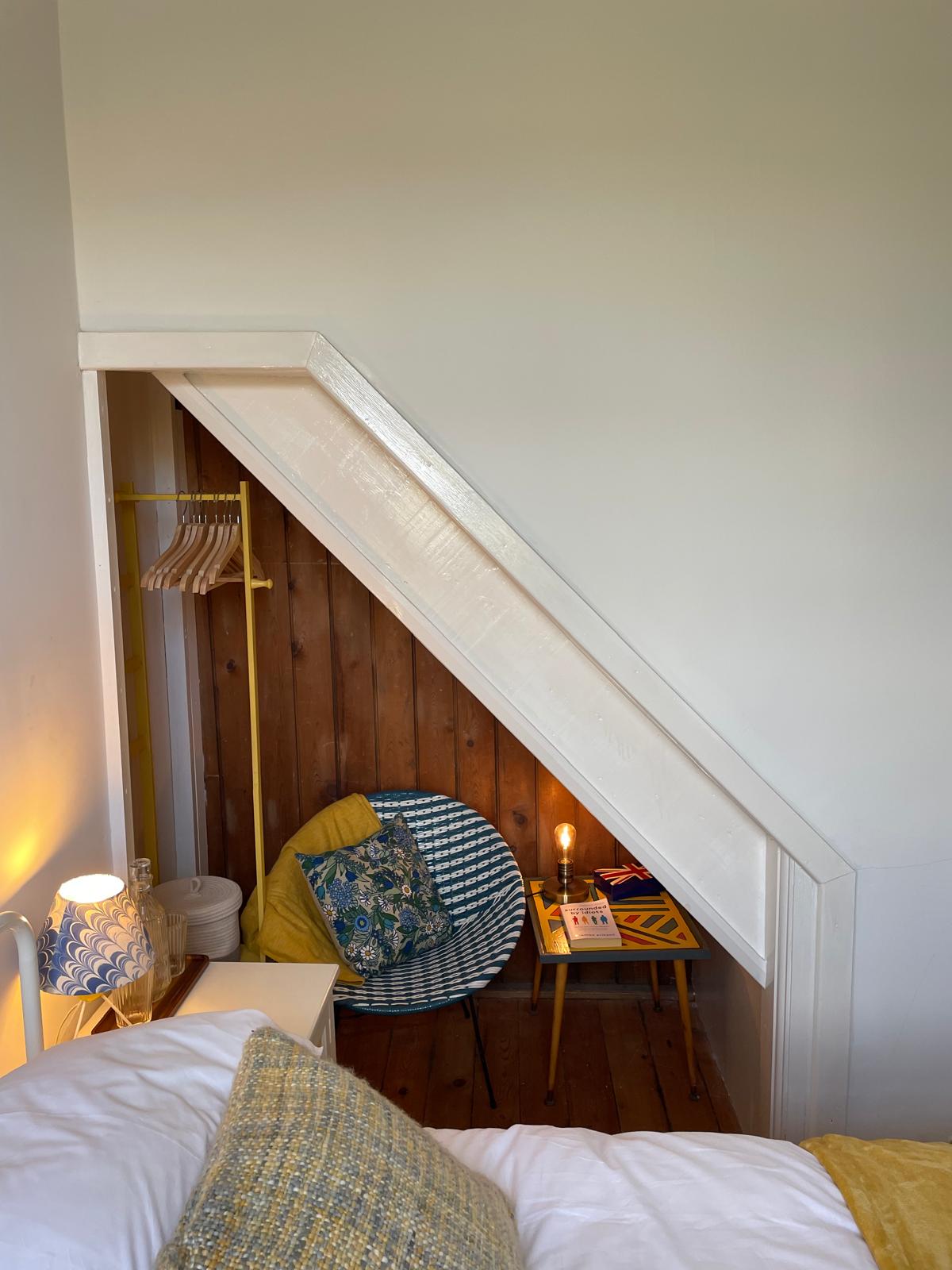 Cozy luxury cottage bedroom featuring a stylish chair, bedside table, and warm lighting under the staircase