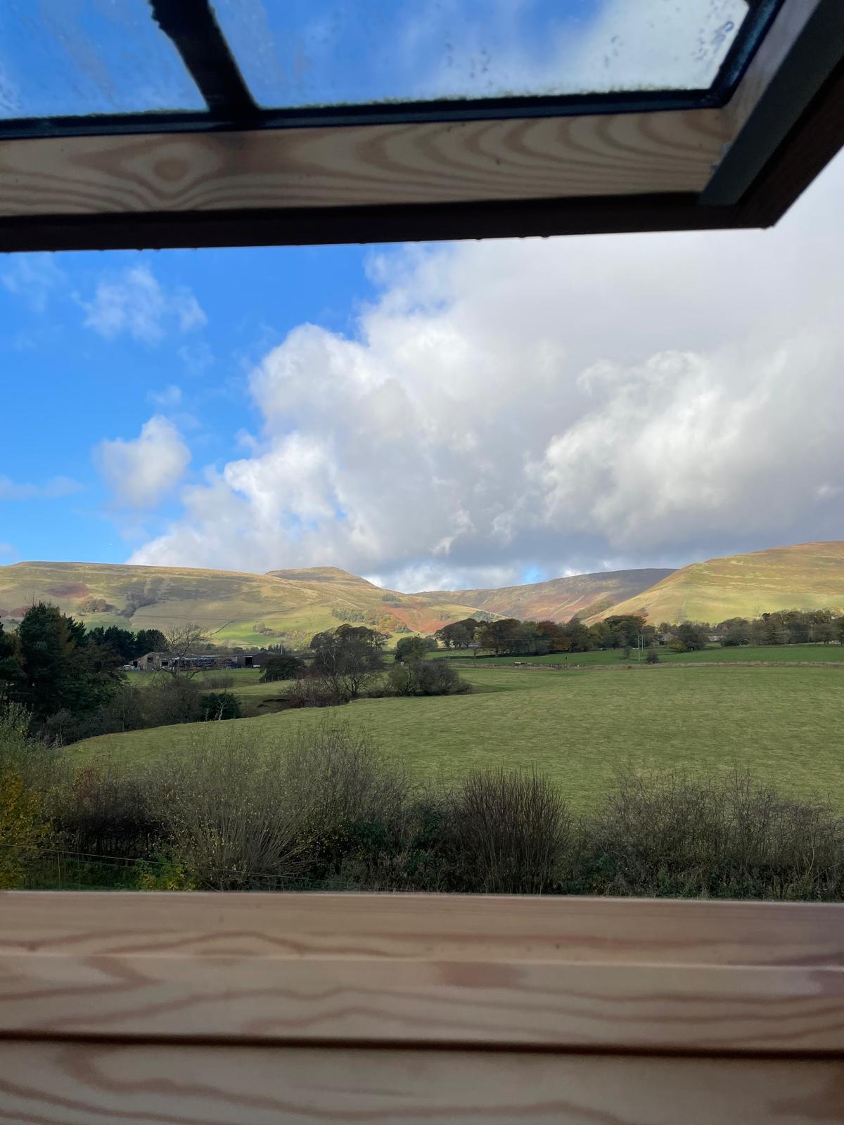 Scenic mountain views from a luxury cottage window, showcasing lush greenery and rolling hills under a blue sky