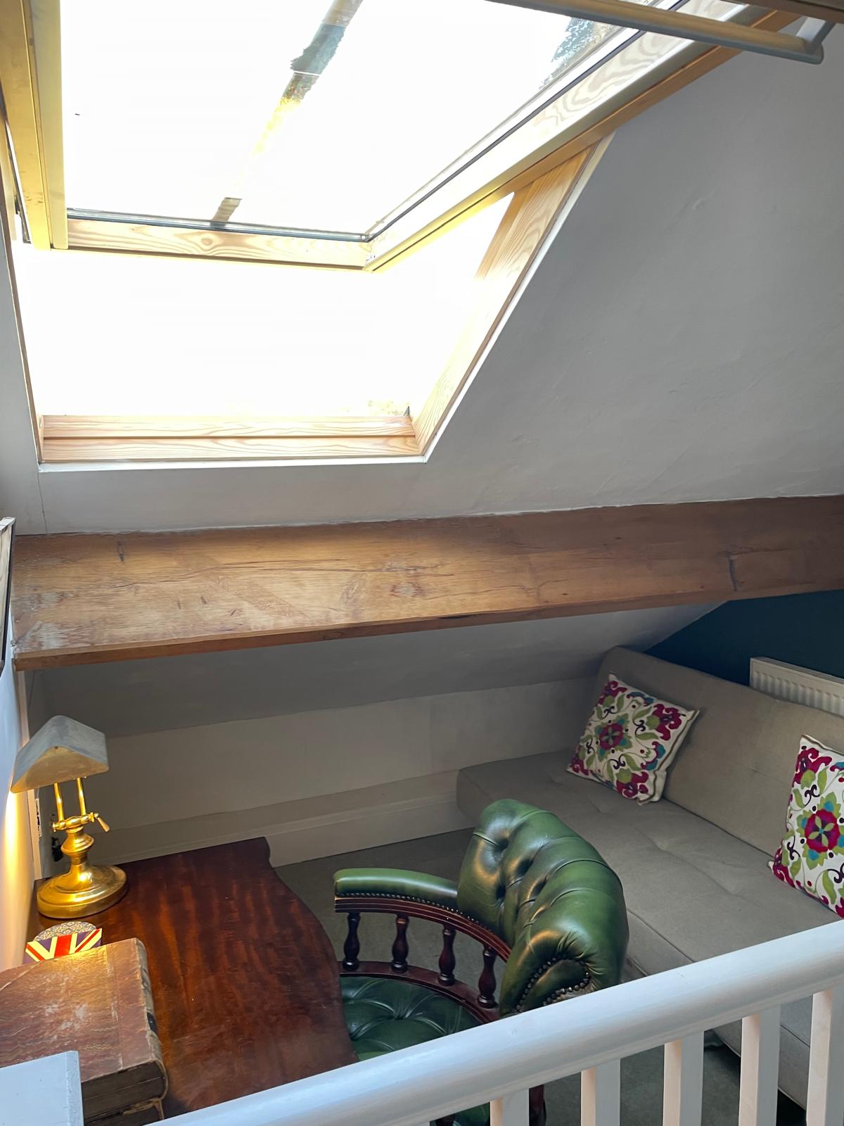 Cozy luxury cottage loft with a skylight, vintage desk, and plush seating, featuring exposed wooden beams and vibrant decor