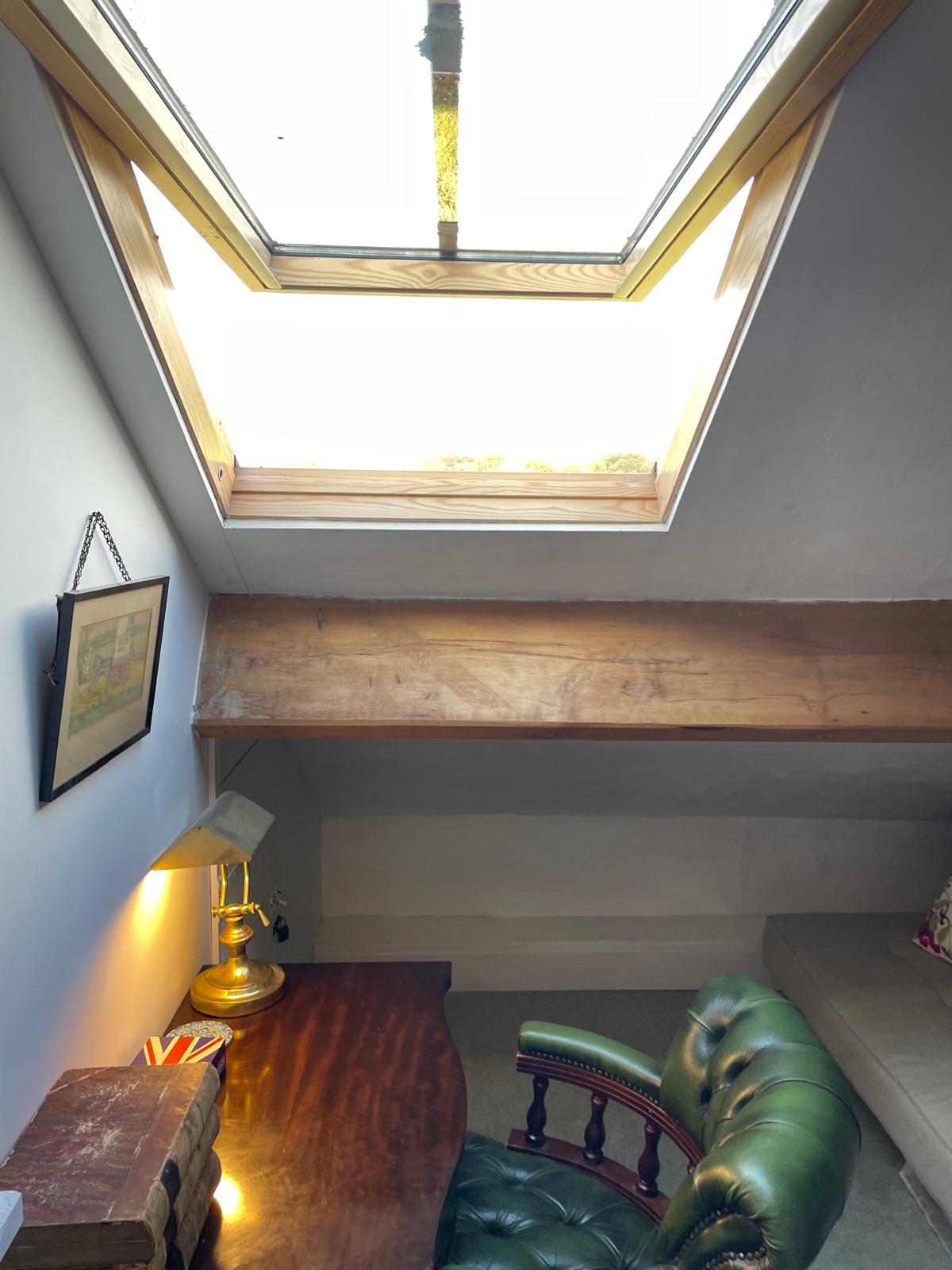 Cozy luxury cottage study with a wooden desk, green leather chair, skylight, and rustic beams