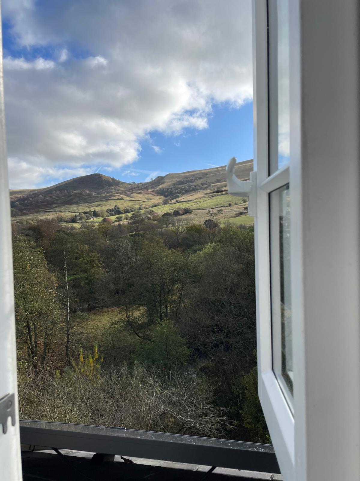 View from a luxury cottage window showcasing lush greenery and rolling hills under a partly cloudy sky