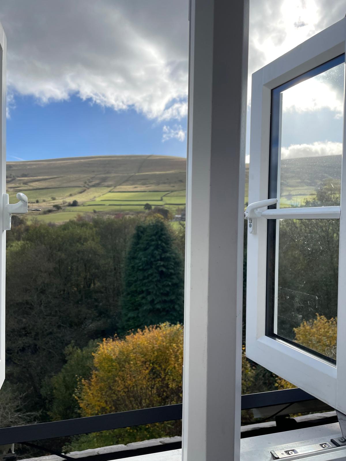 Scenic view from a luxury cottage window, showcasing lush greenery and rolling hills under a bright sky