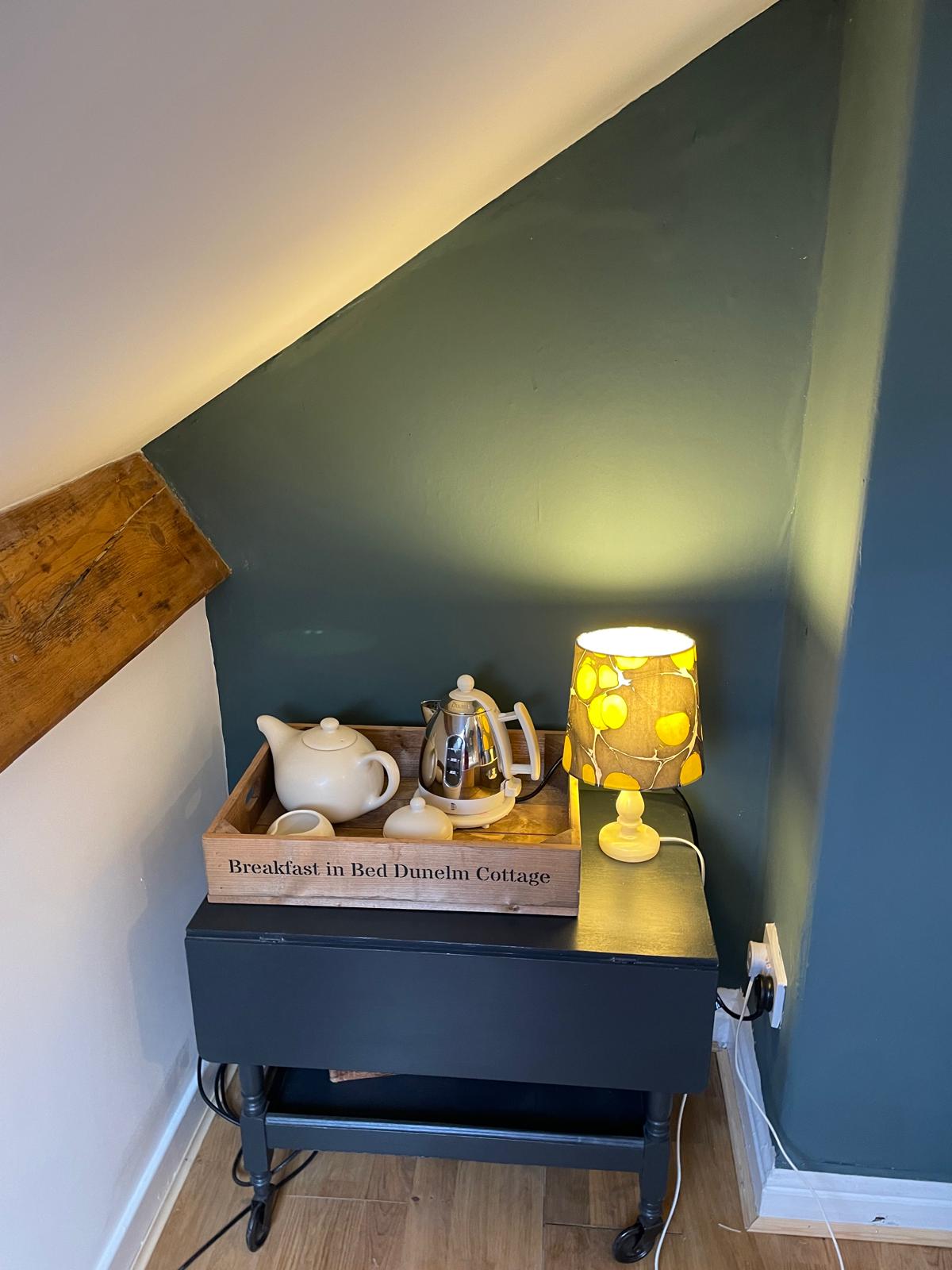 Cozy corner with a tea set, decorative lamp, and wooden accents in a luxury cottage bedroom