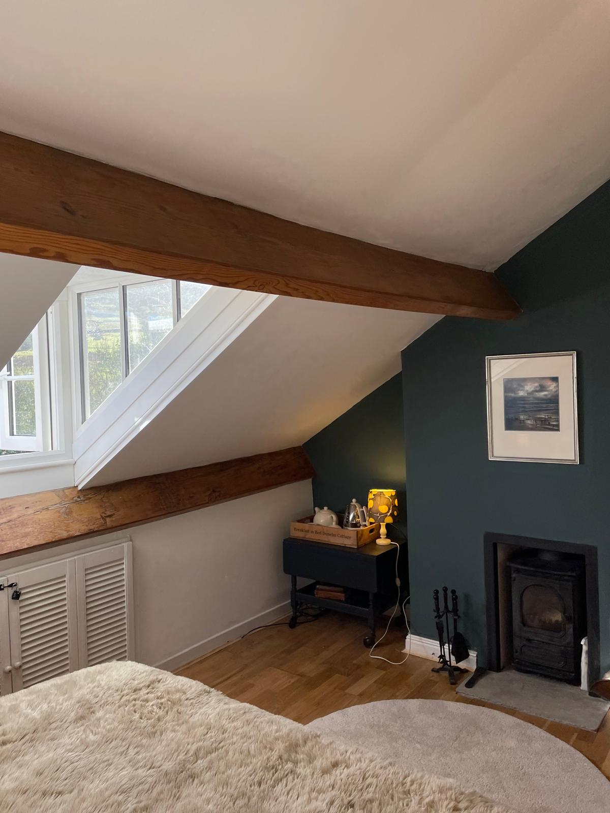 Cozy luxury bedroom with wooden beams, stylish decor, and a fireplace, featuring natural light and warm ambiance
