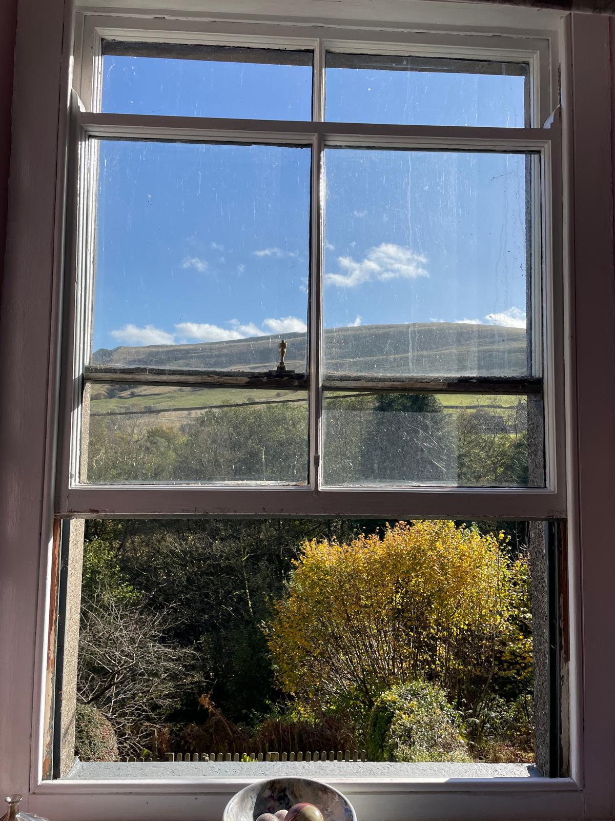 View from a luxury cottage window showcasing lush greenery and rolling hills under a bright blue sky